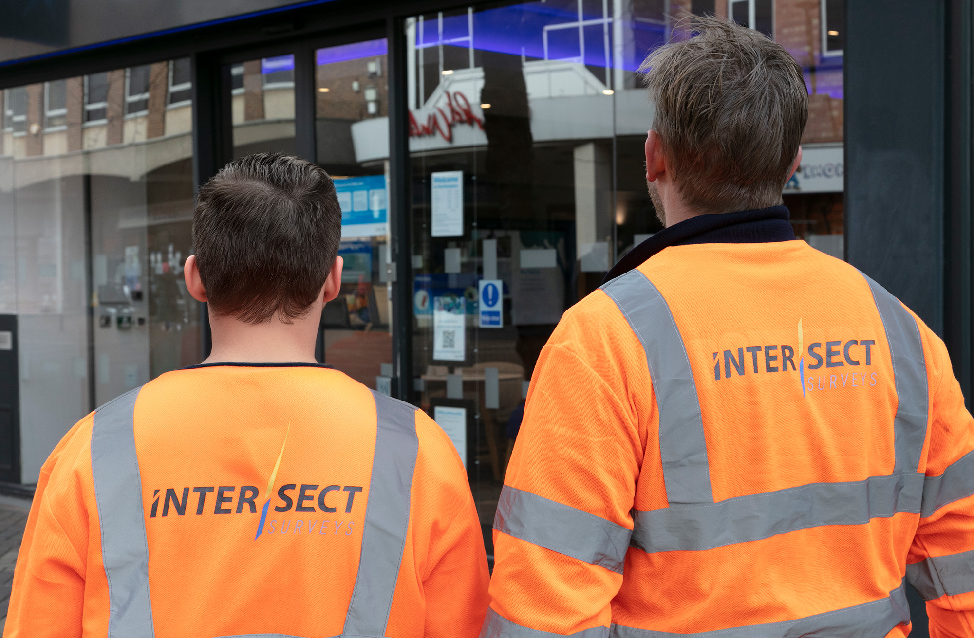 2 workmen in orange hi vis walking away from the camera
